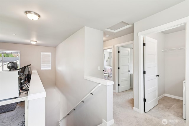 corridor with attic access, light carpet, baseboards, and an upstairs landing