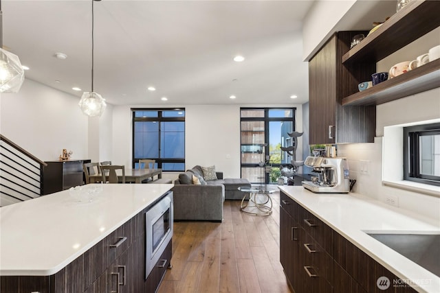 kitchen featuring stainless steel microwave, dark brown cabinetry, light countertops, modern cabinets, and wood-type flooring