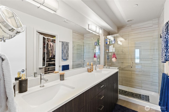 full bathroom featuring a stall shower, double vanity, a sink, and a spacious closet