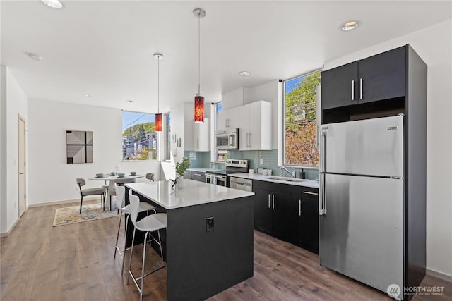 kitchen featuring dark wood finished floors, stainless steel appliances, light countertops, a center island, and hanging light fixtures