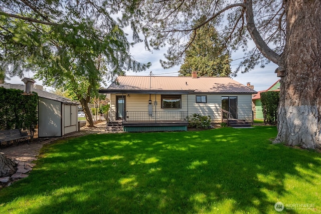 back of house featuring a shed, a chimney, an outdoor structure, a yard, and metal roof