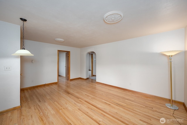 unfurnished room with light wood-style flooring, baseboards, and arched walkways