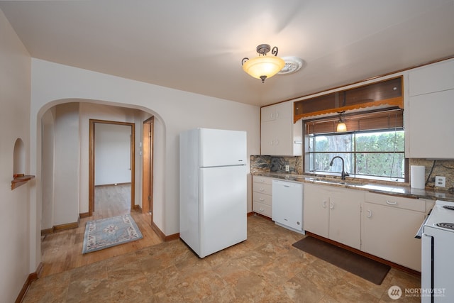 kitchen with backsplash, a sink, arched walkways, white appliances, and white cabinetry