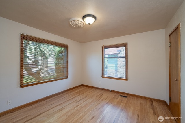 empty room with baseboards, light wood-style flooring, visible vents, and a wealth of natural light