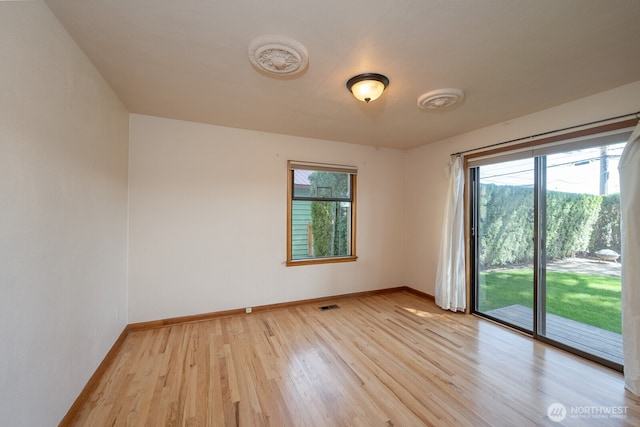 spare room with light wood-type flooring, baseboards, visible vents, and a healthy amount of sunlight
