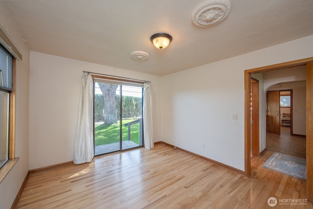 unfurnished room featuring arched walkways, light wood-style floors, and baseboards