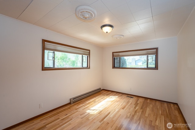 empty room featuring a baseboard heating unit, light wood-style floors, plenty of natural light, and visible vents