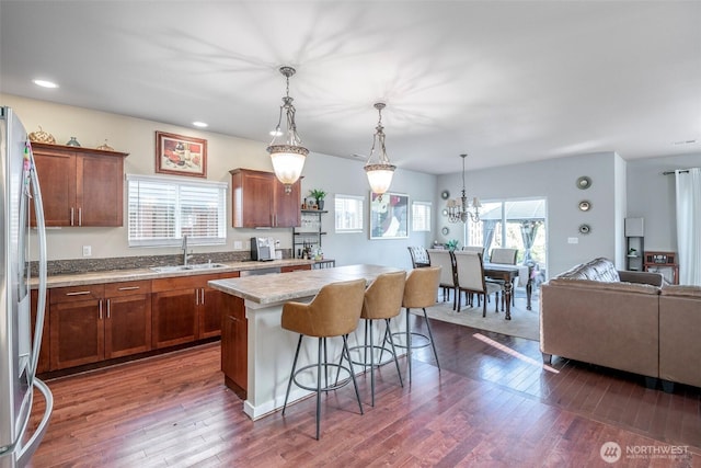 kitchen with a kitchen island, stainless steel refrigerator with ice dispenser, dark wood finished floors, a sink, and a breakfast bar