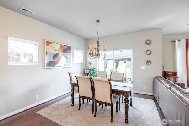 dining area with visible vents, baseboards, wood finished floors, and a chandelier