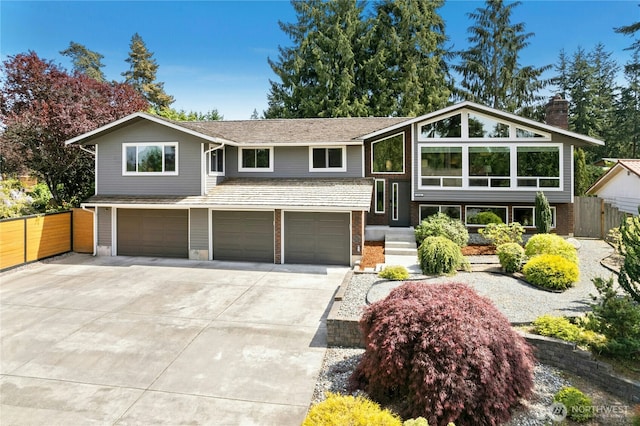 bi-level home with an attached garage, fence, driveway, a chimney, and brick siding