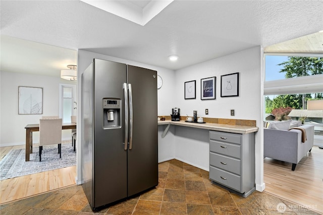 kitchen with stainless steel fridge, gray cabinets, baseboards, and an office area