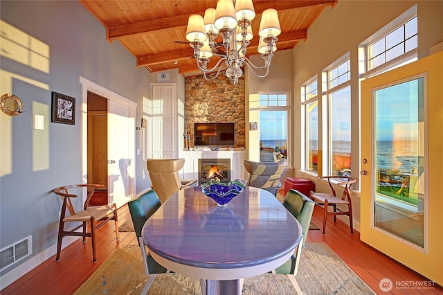 dining space with hardwood / wood-style floors, a towering ceiling, an inviting chandelier, visible vents, and wooden ceiling
