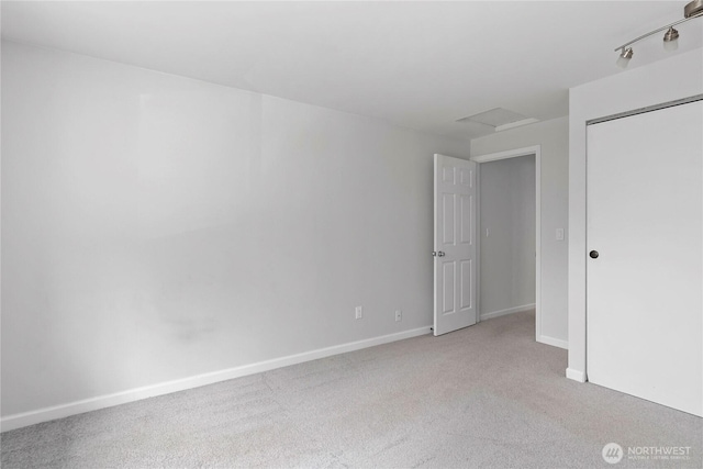 unfurnished bedroom featuring light carpet, a closet, attic access, and baseboards