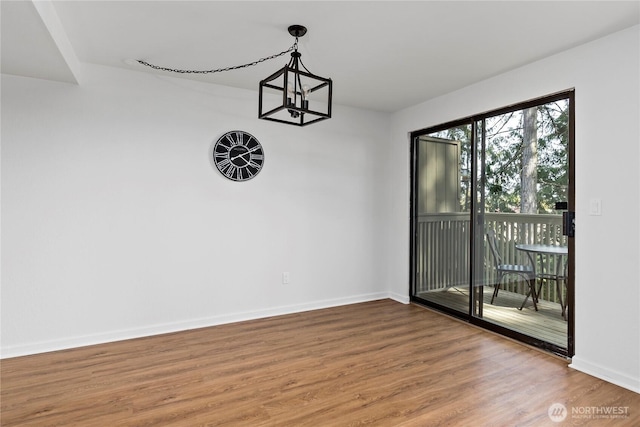 unfurnished dining area featuring a notable chandelier, baseboards, and wood finished floors