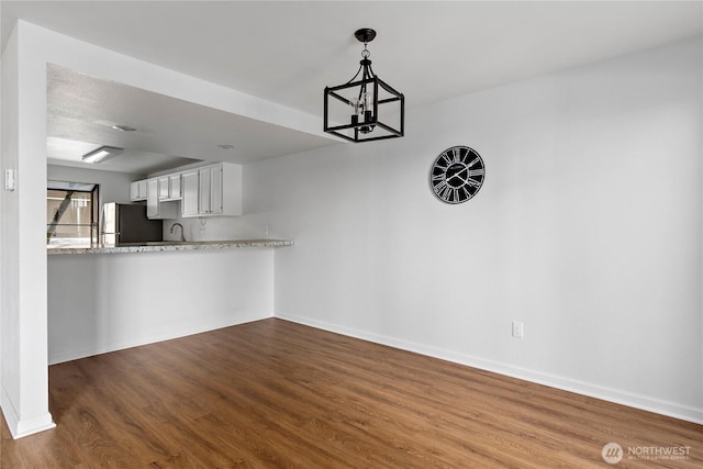 unfurnished dining area with a chandelier, dark wood-style floors, baseboards, and a sink