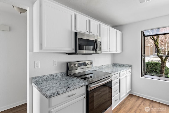 kitchen featuring light wood finished floors, baseboards, white cabinets, and stainless steel appliances