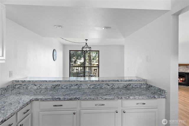 kitchen with light stone counters, a peninsula, white cabinets, pendant lighting, and wood finished floors