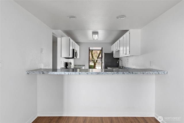 kitchen with wood finished floors, a sink, white cabinets, and stainless steel appliances