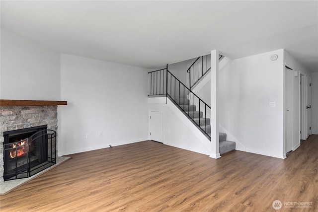 unfurnished living room with baseboards, stairway, wood finished floors, and a fireplace