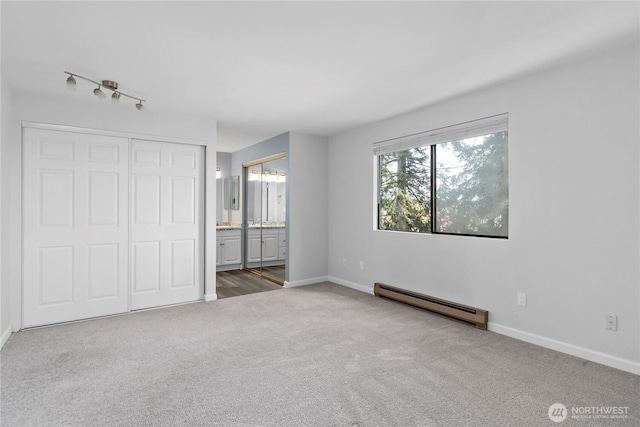 unfurnished bedroom with ensuite bathroom, baseboards, carpet, a closet, and a baseboard radiator