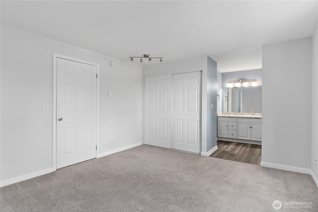 unfurnished bedroom with dark carpet, a closet, ensuite bathroom, and baseboards
