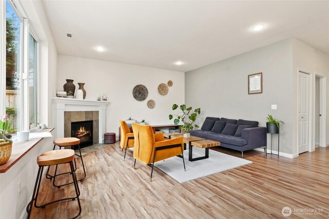 living room featuring a tiled fireplace, recessed lighting, baseboards, and light wood finished floors