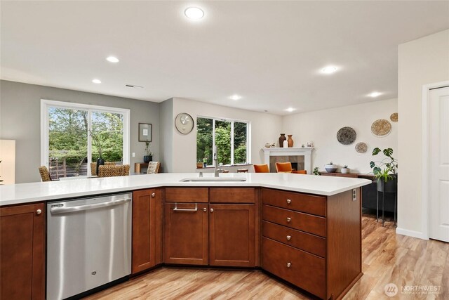kitchen with stainless steel dishwasher, light wood-style floors, a sink, and light countertops