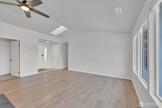 interior space with vaulted ceiling with skylight, a textured ceiling, a ceiling fan, visible vents, and light wood finished floors