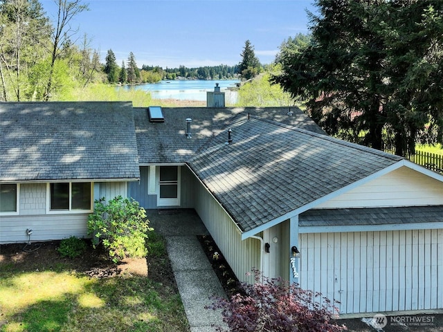 view of side of home with a chimney, a shingled roof, and a water view