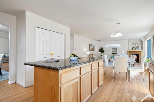 kitchen featuring open floor plan, light brown cabinets, dark stone countertops, and light wood-style floors