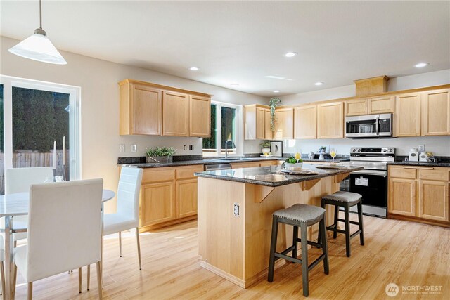 kitchen with light wood finished floors, a kitchen breakfast bar, light brown cabinetry, a kitchen island, and appliances with stainless steel finishes