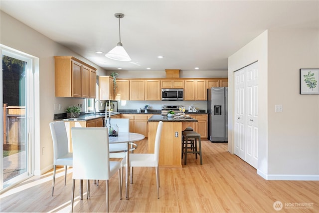 kitchen with dark countertops, stainless steel appliances, light brown cabinetry, and light wood-type flooring
