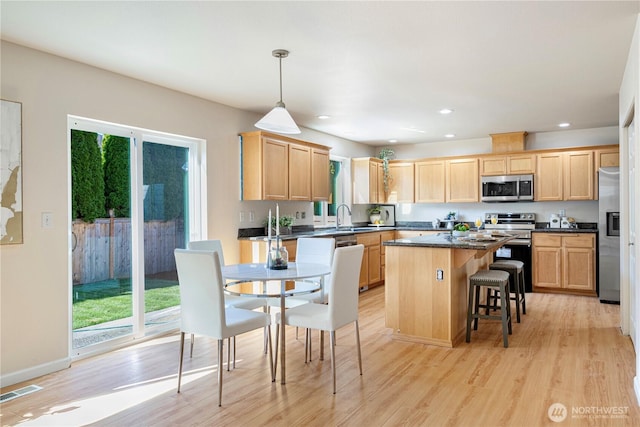 kitchen with light wood-style flooring, light brown cabinetry, a sink, a kitchen island, and appliances with stainless steel finishes