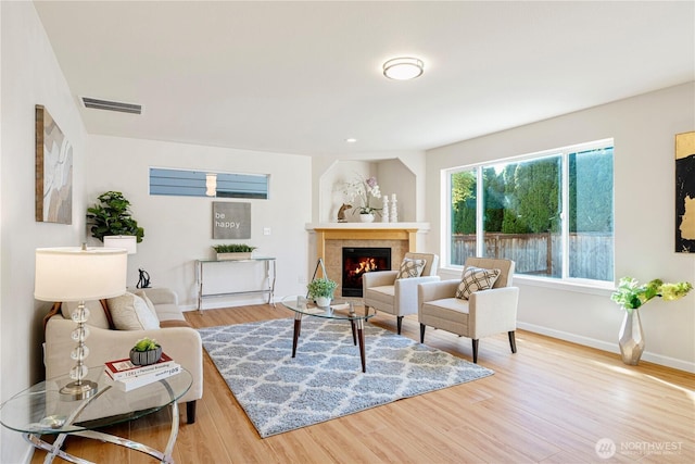 living area with baseboards, wood finished floors, visible vents, and a tiled fireplace
