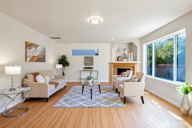 living area featuring baseboards, wood finished floors, visible vents, and a tiled fireplace