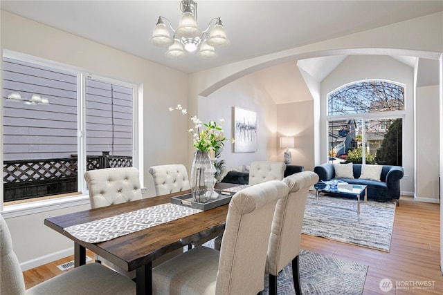 dining room featuring a chandelier, arched walkways, light wood finished floors, baseboards, and lofted ceiling