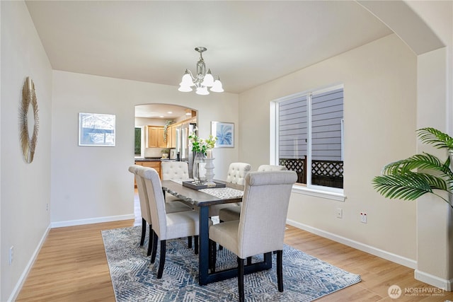 dining area with arched walkways, a chandelier, light wood finished floors, and baseboards