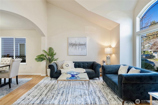 living area featuring arched walkways, wood finished floors, baseboards, and high vaulted ceiling