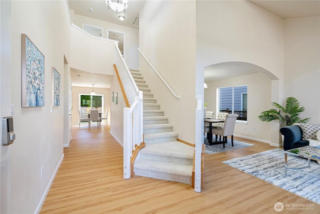 stairway featuring arched walkways, a towering ceiling, wood finished floors, and baseboards