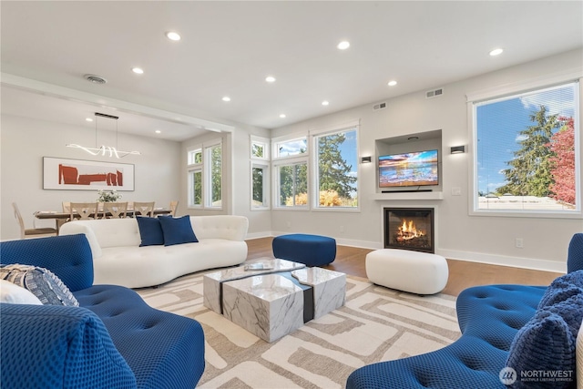 living area featuring visible vents, wood finished floors, a glass covered fireplace, and recessed lighting