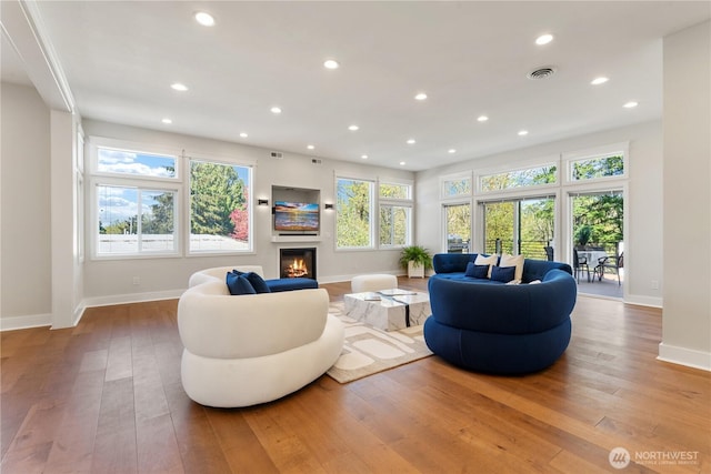 living room with recessed lighting, hardwood / wood-style flooring, baseboards, and a glass covered fireplace