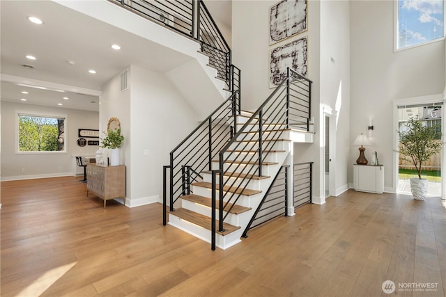 staircase with wood finished floors, a towering ceiling, visible vents, recessed lighting, and baseboards