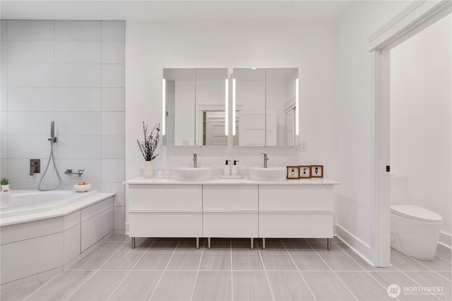 full bath with toilet, a bath, double vanity, and a sink