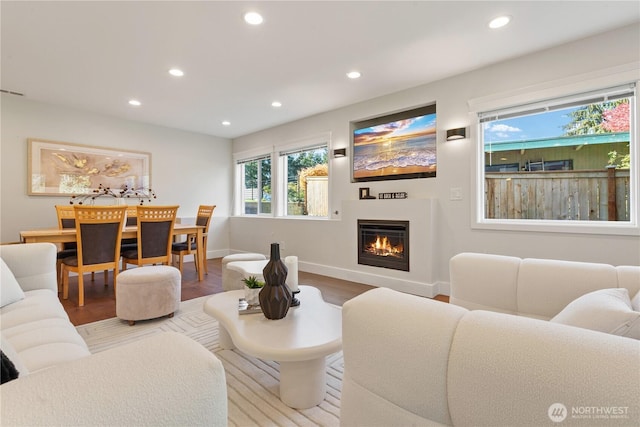 living area featuring wood finished floors, baseboards, a glass covered fireplace, and recessed lighting