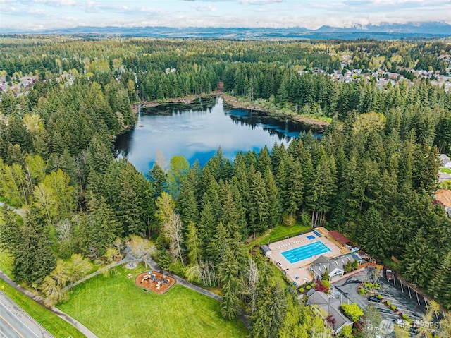 bird's eye view of a heavily wooded area, a nearby body of water, and a pool