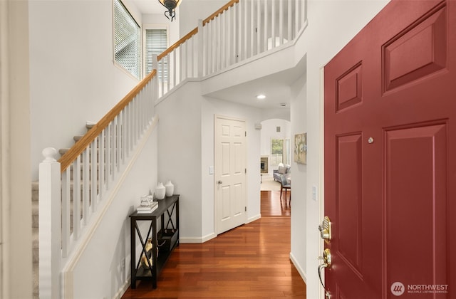 entryway featuring dark wood-style floors, a towering ceiling, stairway, arched walkways, and baseboards