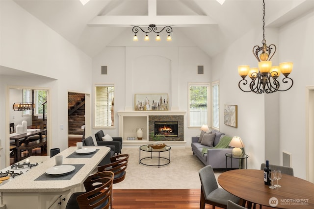 living room with a chandelier, wood finished floors, beamed ceiling, high vaulted ceiling, and a warm lit fireplace