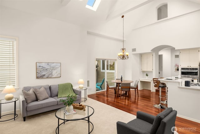 living area with high vaulted ceiling, a chandelier, arched walkways, a skylight, and wood finished floors