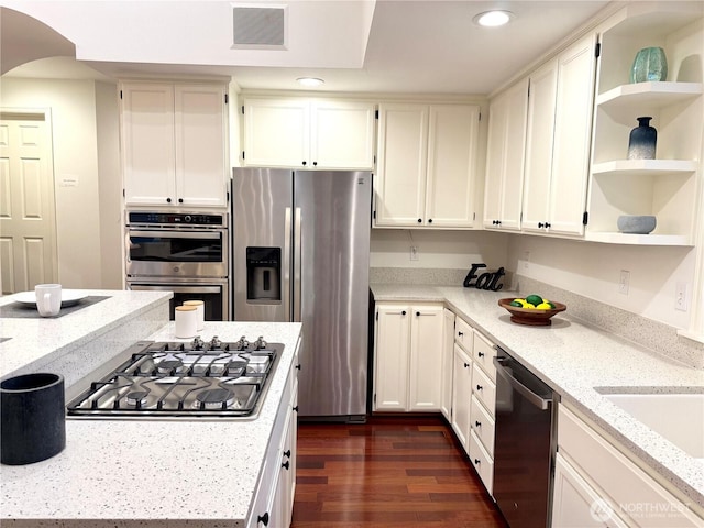 kitchen featuring appliances with stainless steel finishes, open shelves, recessed lighting, light stone counters, and arched walkways