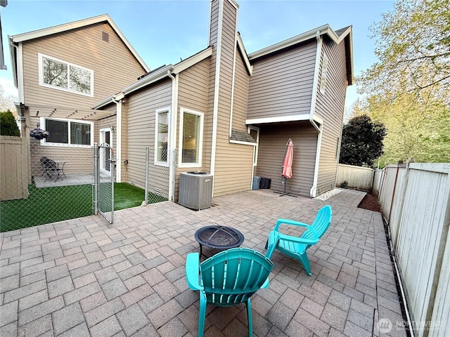 back of house with a fire pit, cooling unit, a patio, a chimney, and a fenced backyard